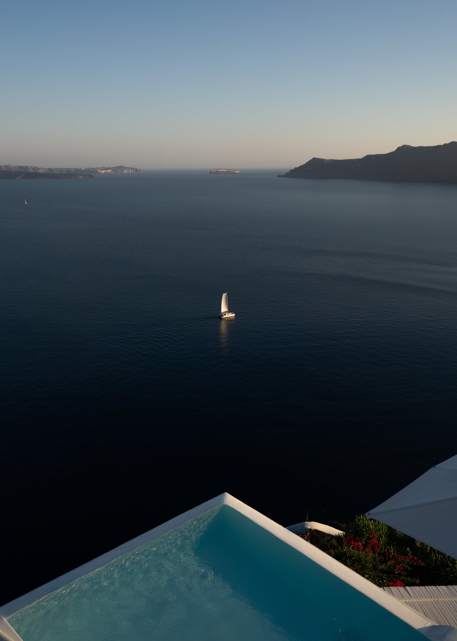 A sailboat catching the last sun on a dark sea, seen from above a pool.
